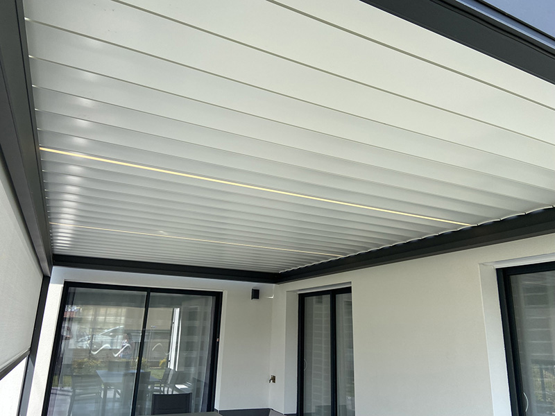 Pergola bioclimatique en aluminium de couleur gris foncé avec 2 lames LED et 1 store screen en façade