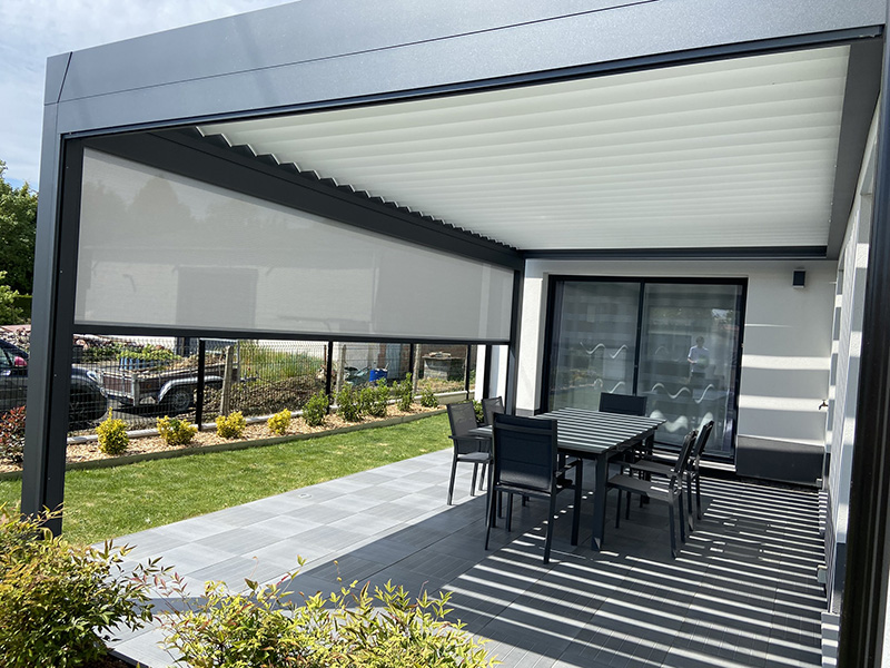 Pergola bioclimatique en aluminium à lames orientables de couleur gris foncé et store Fixscreen en façade.