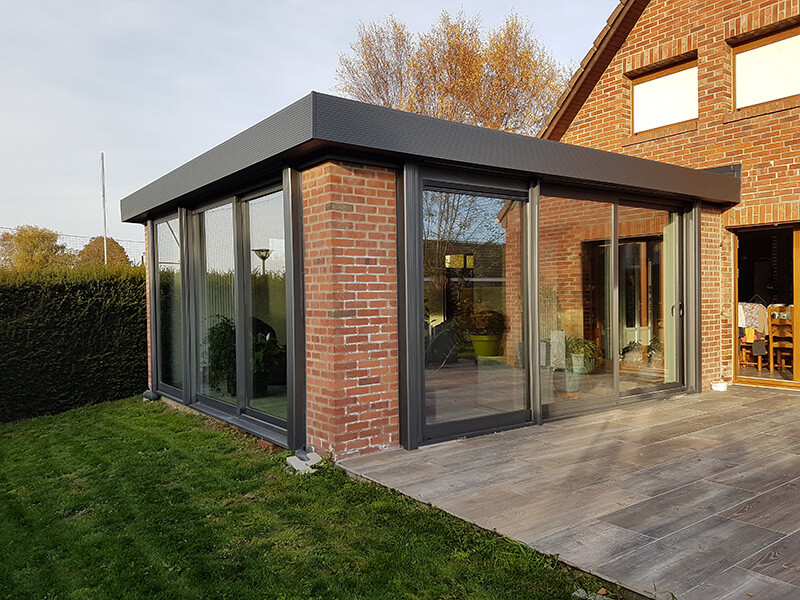 Extension d'habitation de type toiture plate de couleur gris foncé avec murs en briques  identiques à celles de la maison