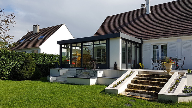 Véranda de type toiture plate de couleur gris foncé avec dôme mono-pente, chéneau plat contemporain et impostes vitrées