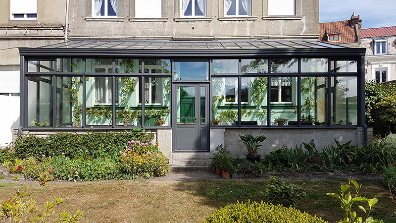 Véranda mono-pente de couleur gris foncé de style atelier avec toiture vitrée et chéneau mouluré